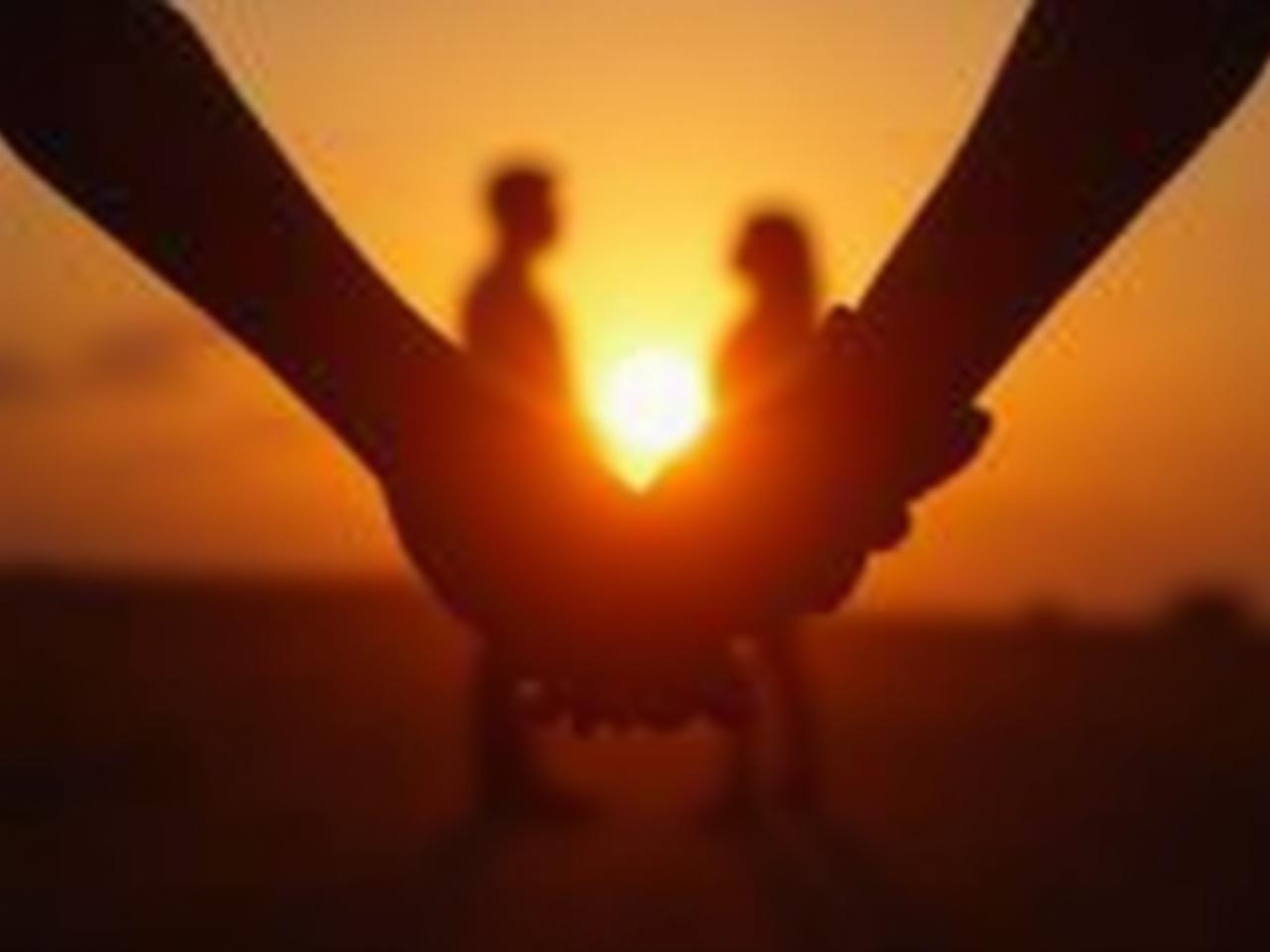 A couple holding hands intimately while looking at a sunset. The image represents connection, love, and the beauty of intimacy.
